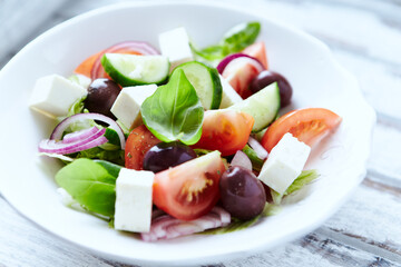 Healthy salad with feta cheese, kalamata olives, cherry tomatoes and fresh basil. Bright wooden background. Close up. 	