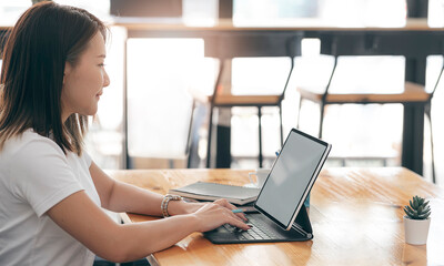 Young beautiful asian woman working on tablet computer while sitting at co-workspace.