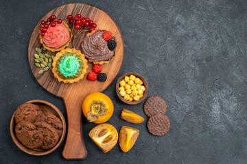 top view delicious little cakes with biscuits and fruits on dark desk sweet pie cake