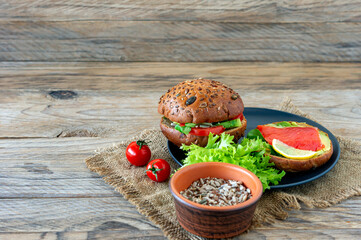 Homemade Organic Salmon Burger with tomato, corn salad and avogado on a plate on wooden backgound. Healthy organic food.
