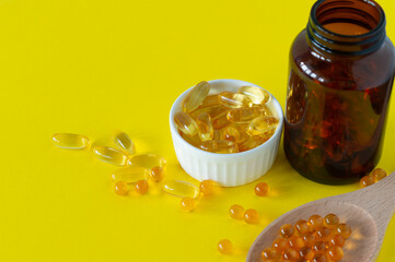 Fish oil capsules on yellow background, vitamin D, omega supplement, selective focus.