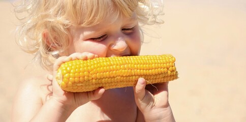 Little blond boy eating boiled corn on the beach. Healthy food, summertime, vacation banner.	