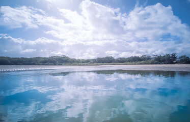 Beautiful cloud reflections on the calm waters of a coastal river at low tide.