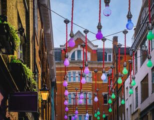 View of street in London, England, with brick buildings at sunset; street is decorated with colorful bulbs