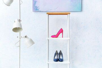 Stand with stylish female shoes and lamp near light wall
