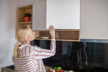 Blonde woman opening the cupboard in the kitchen