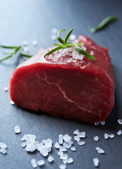 Fresh raw beef steak with herbs and spices. Dark stone background. Close up. 