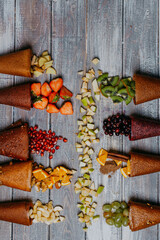 Fruit leather cones with fresh fruits in pieces on the wooden table. No sugar fruit leather cones. Healthy food. Apples, bananas, strawberries, oranges, nuts, black currant, pomegranate top view.