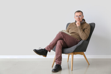 Male psychologist sitting in armchair near light wall