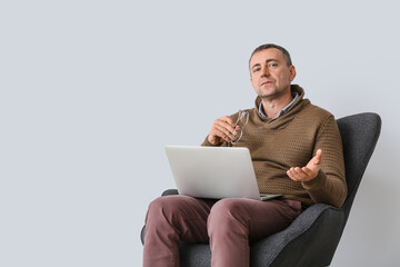 Male psychologist with laptop sitting in armchair near light wall