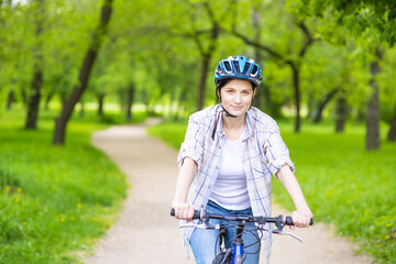 Girl in a bicycle helmet oclocotilas on a bicycle handlebar and looks at the camera on a path in a summer park