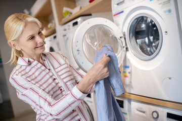 Blonde woman in striped shirt sitting on a washing machine and holding a towel