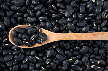 Black beans on a wooden spoon, and some on the white floor.