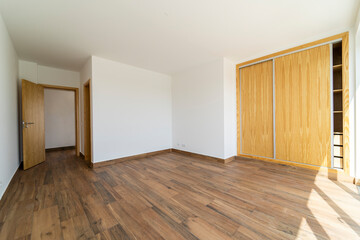 Empty room with dark wooden floating laminate flooring. House interior, wide bedroom or living room space. Newly recently painted new apartment or house. Wood floor. Real state or property management