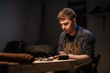 a young talented shoemaker in the workshop is engaged in manual production of shoes made of leather