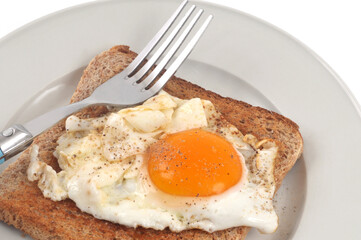 Oeuf au plat sur une tranche de pain de mie dans une assiette avec une fourchette en gros plan sur fond blanc