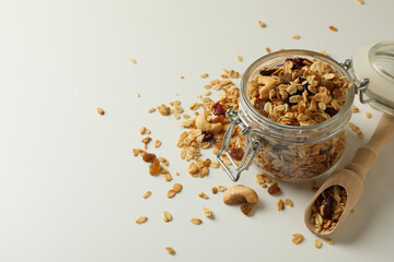 Glass jar and scoop with granola on white background