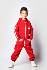 Male school student model showing warm red jumpsuit for camera, standing against studio wall background. Warm fashion clothes for winter or autumn advertising