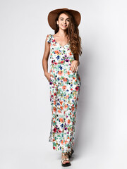 Luxurious young slim girl with long hair in a long dress with a floral print and a straw hat....