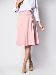 Cropped photo of young woman, posing in isolation, in an official light blouse, pink skirt and high-heeled shoes