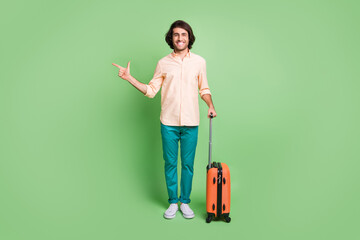 Full length body size view of funny cheerful guy departing holding bag demonstrating copy space isolated over bright green color background