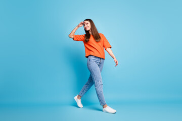 Full length photo of toothy beaming girl dressed red t-shirt walking looking back arm forehead isolated blue color background