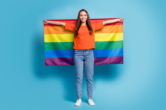 Full length photo of cheerful lesbian woman wearing casual red t-shirt holding hands arms lgbt flag isolated blue color background