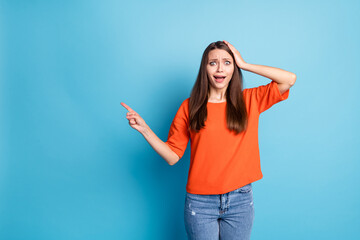 Photo of funny shocked young woman wearing casual jeans orange t-shirt pointing one finger empty space arm head isolated blue color background