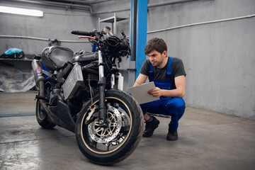Fototapeta na wymiar A Workshop worker inspects a motorcycle. He is wearing a blue overalls