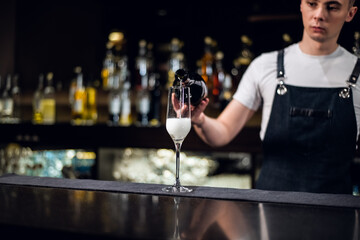 an experienced bartender in an apron fills a glass of champagne at the bar.