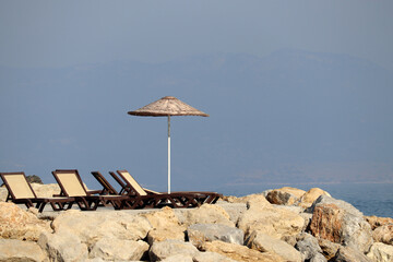 Empty deck chairs and sun umbrella on a stone beach on misty mountains background. Beach vacation...