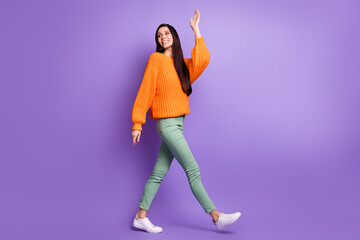 Full length body size photo of young girl walking forward waving hand looking back isolated on bright violet color background