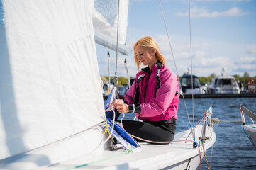 Young athletic girl in sports clothes on a yacht in the dock is ready for a sailing regatta