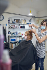 Hairdresser and customer in a salon with medical masks during virus pandemic. Working with safety mask.