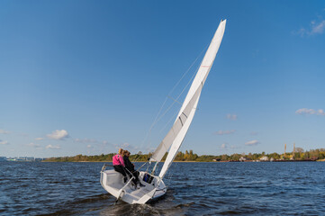 A young sailing instructor conducts a class with two female novices on a river with a beautiful...