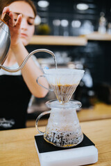 The girl brews coffee through a filter in a drip method and pours it into a glass cup