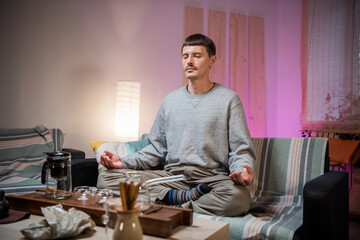 Meditating man on the sofa in the interior of the house. Complete immersion in the art of tea...