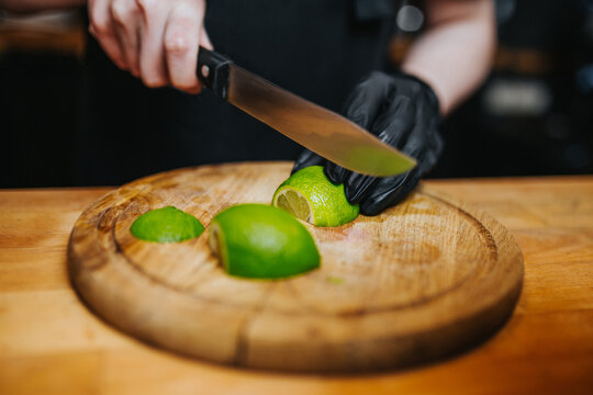 Slicing lime into cocktail slices - kitchen cutting board - black rubber gloves - Powered by Adobe