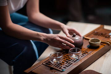 The girl is holding a ceramic teapot. Close-up of a table for a ritual tea party in China. Bamboo table with tray and cups