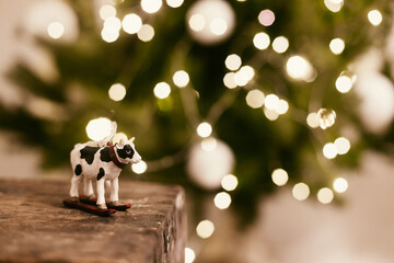 Symbol of new year 2021 cow or bull toy on background of beautiful christmas tree lights bokeh, space for text. Cute cow figurine decor on christmas tree. Happy New Year 2021 !