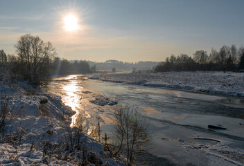The sun sets over a frozen river on a winter evening