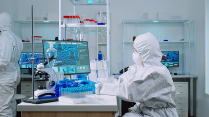Fototapeta na wymiar Woman biochemist in coverall checking manifestations of virus working on comuper in equipped lab. Team of doctors examining vaccine evolution using high tech researching diagnosis against covid19
