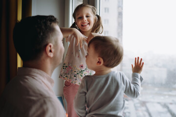 kids can't wait to go outside during coronavirus pamdemia. Standing on window sill and having fun with father looking outside