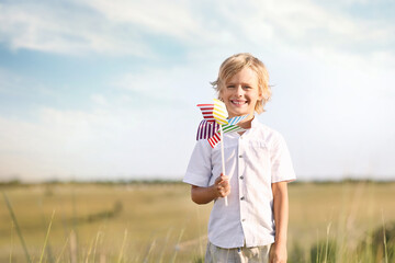 Cute little boy with pinwheel outdoors, space for text. Child spending time in nature