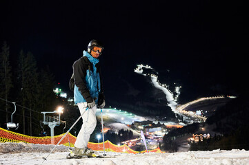 Male skier in winter ski jacket and helmet holding ski poles. Young man standing on snow-covered...