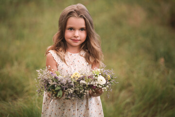 Naklejka premium Cute little girl holding wreath made of beautiful flowers in field