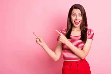 Photo of amazed brown haired girl point fingers empty space wear red striped t-shirt isolated on vivid pink color background