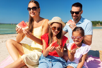family, leisure and people concept - happy mother, father and two daughters having picnic on summer beach and eating watermelon