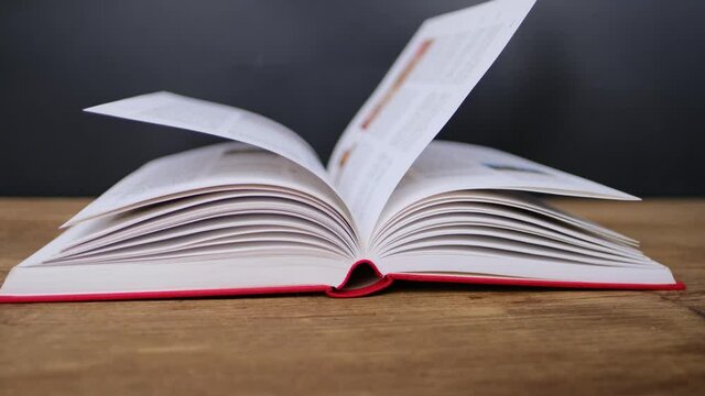 open paper book with red cover lies on a wooden table closeup, hand flipping pages, reading concept