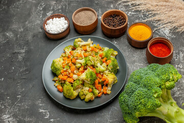 Top view of set of different spices in brown bowls and vegetable salad on gray table